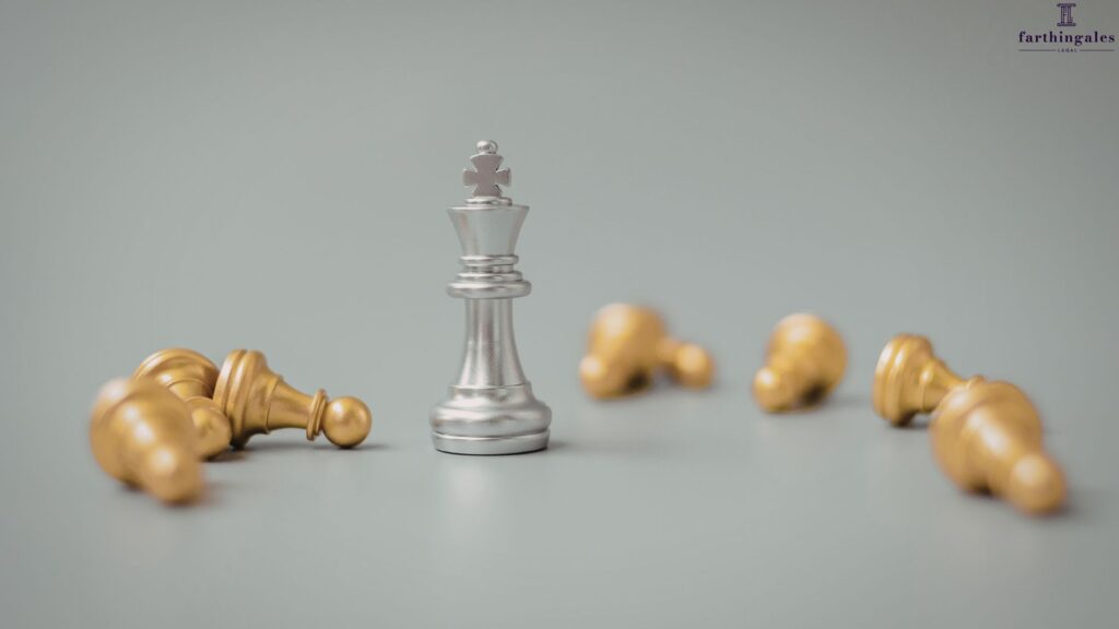 A silver king chess piece standing upright amidst several fallen gold chess pawns on a grey surface.